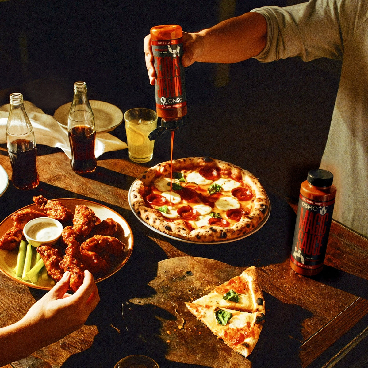 Pouring Magic Sauce over pizza next to wings