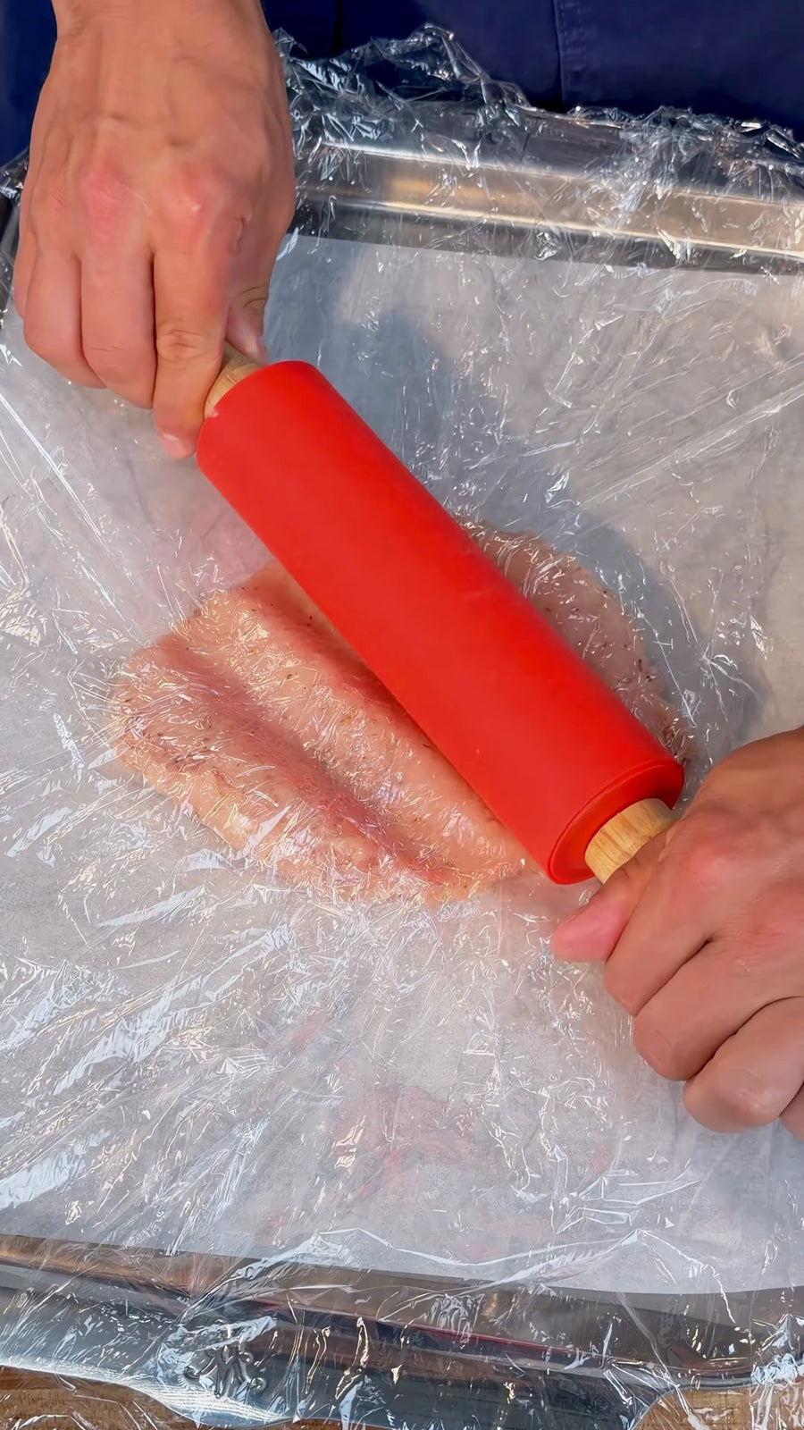 Nick rolls the chicken thin under a clear plastic covering.
