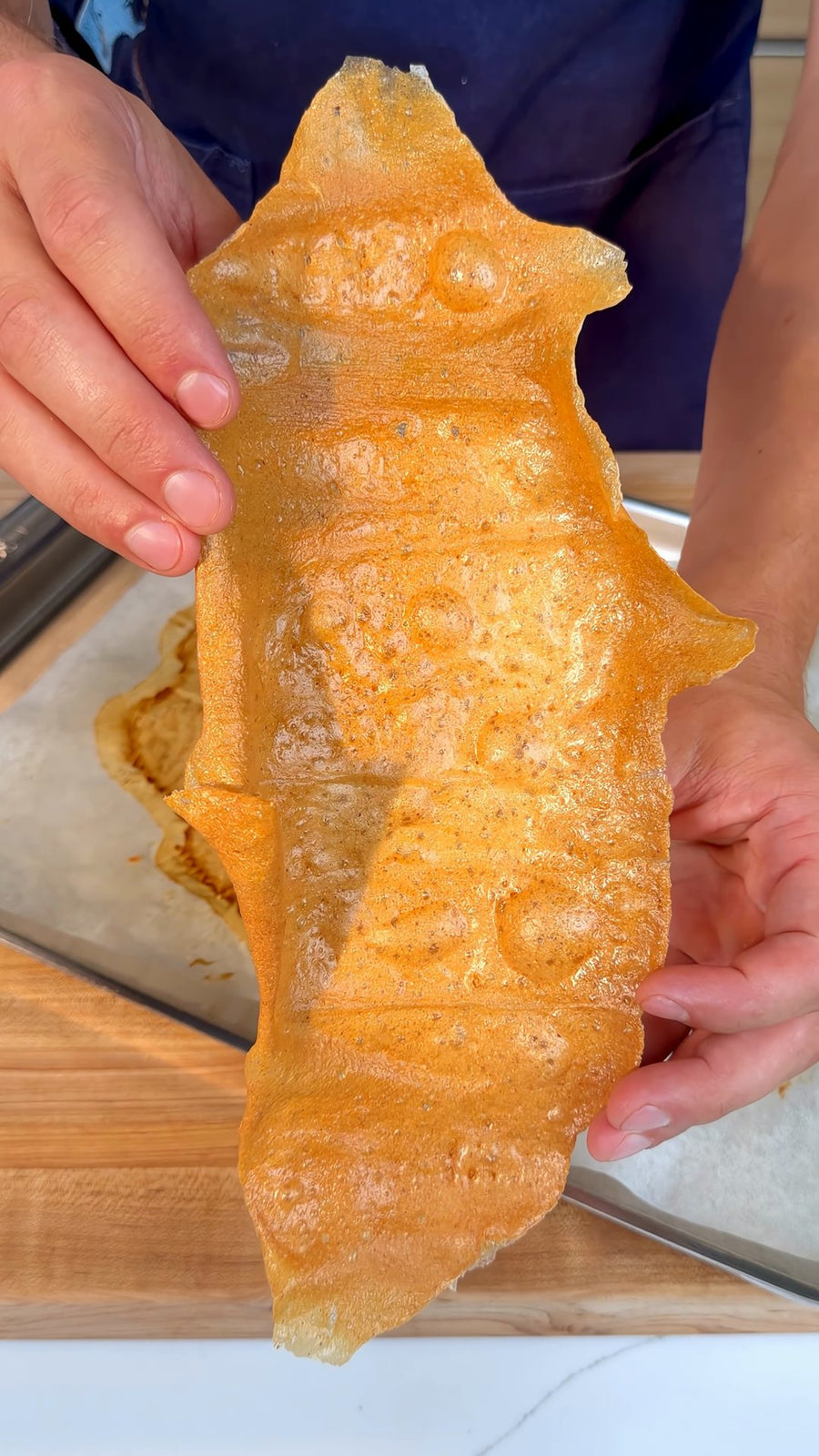 Nick holds a crisp piece of the baked chicken chip above the tray.