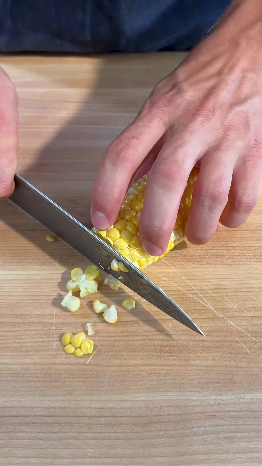 Nick trims the end from a corn cob on the cutting board.