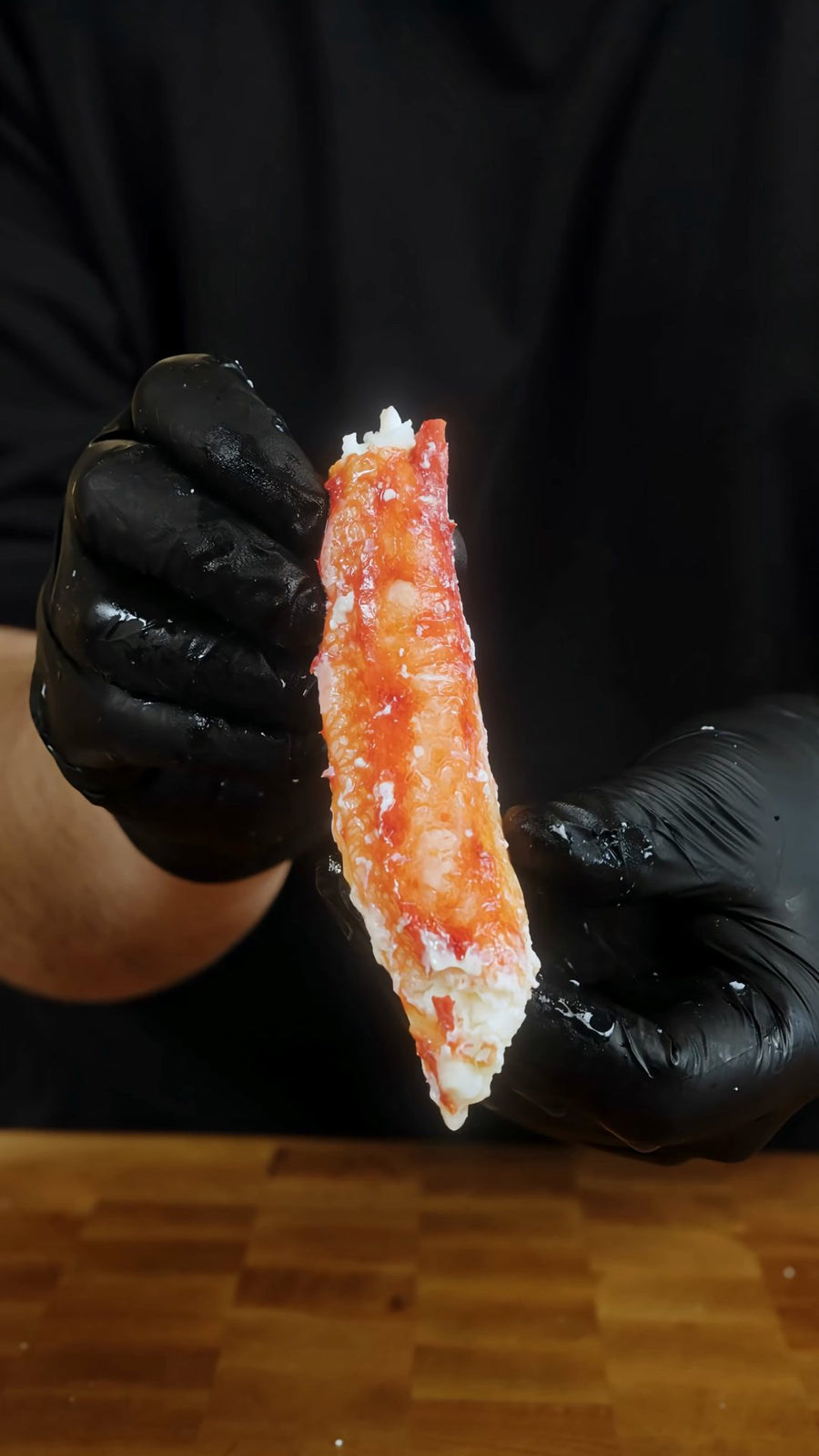 Cooked crab meat is pulled from a crab leg with gloved hands.