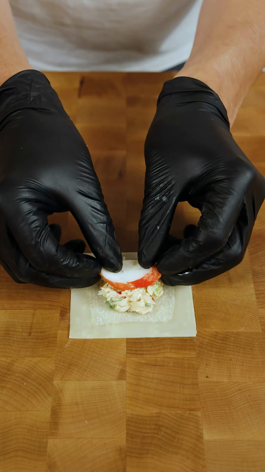 A slice of imitation crab is placed on a mound of filling in a wonton wrapper.