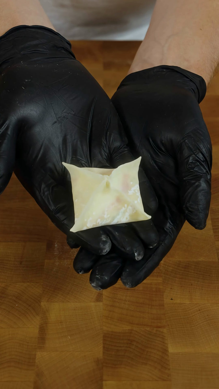 Gloved hands hold a sealed, square crab rangoon pillow.