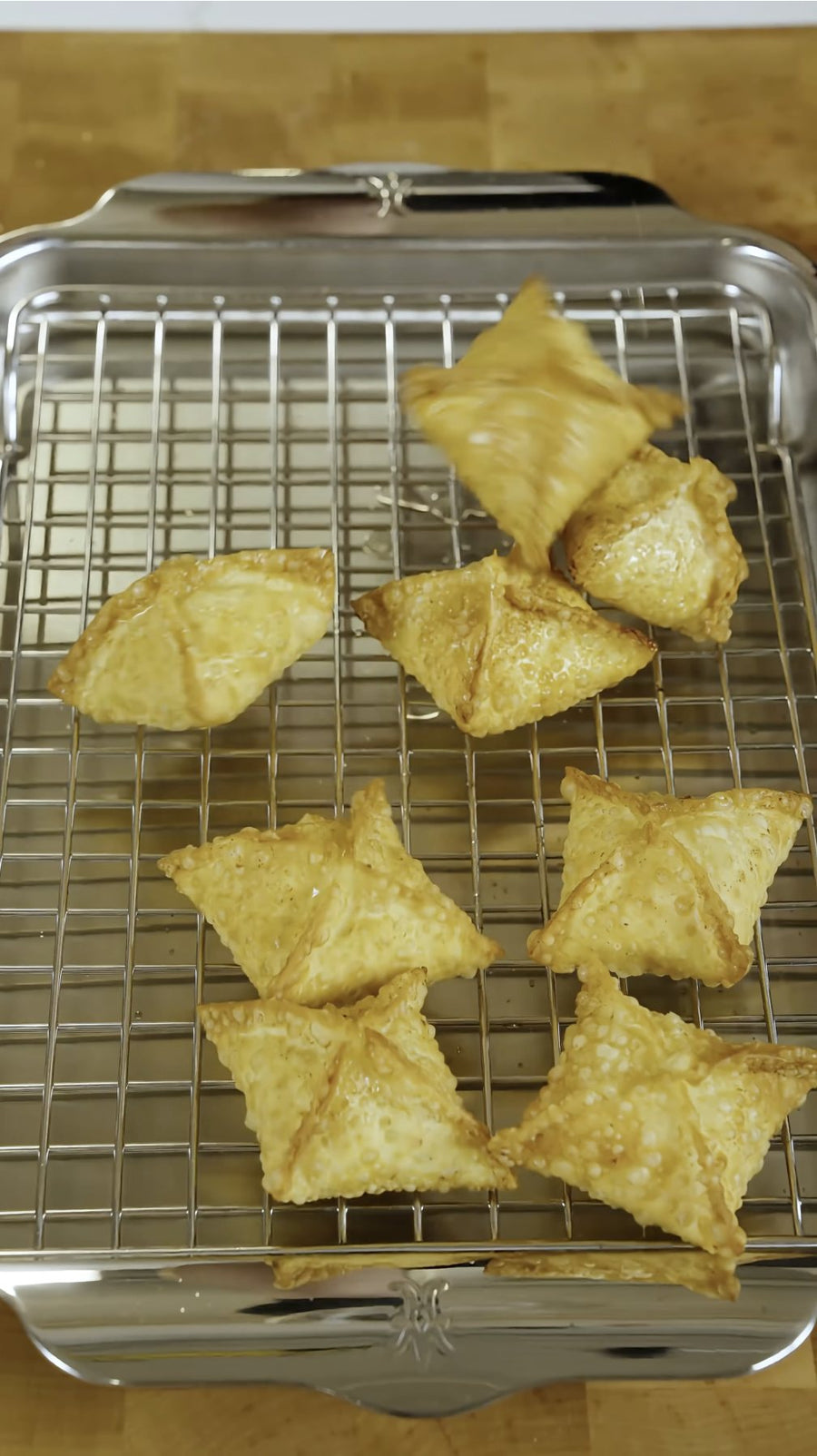 Golden crab rangoon drain on a wire rack over a baking sheet.
