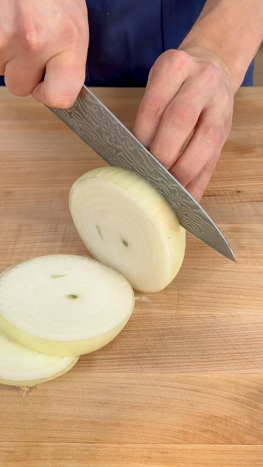 Nick slices a yellow onion into thick rings.