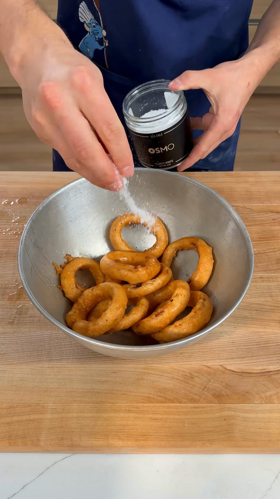Nick holds the Osmo Flakey White Sea Salt tin while seasoning the hot onion rings.